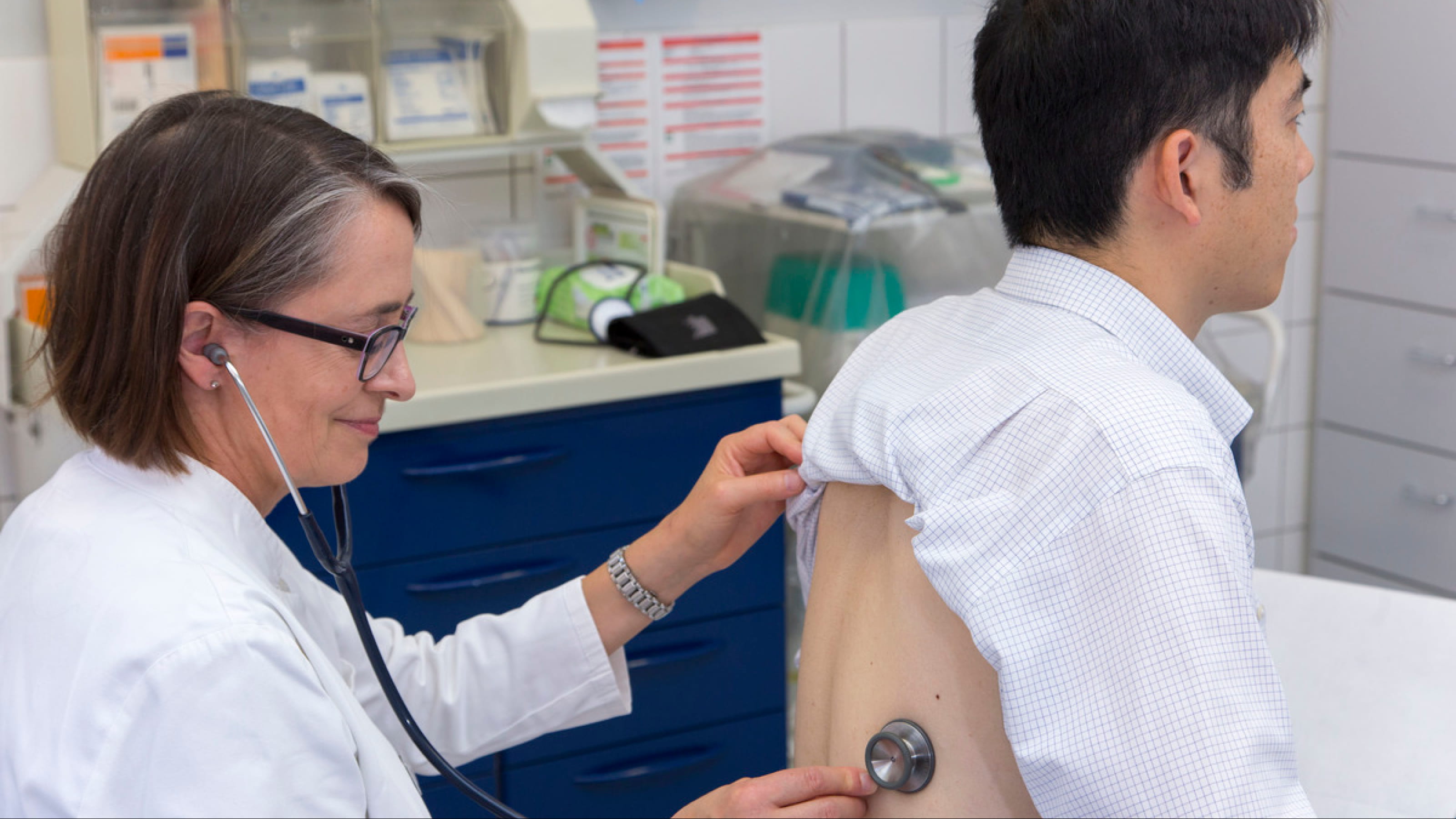 Docteure auscultant un patient par le dos dans une clinique