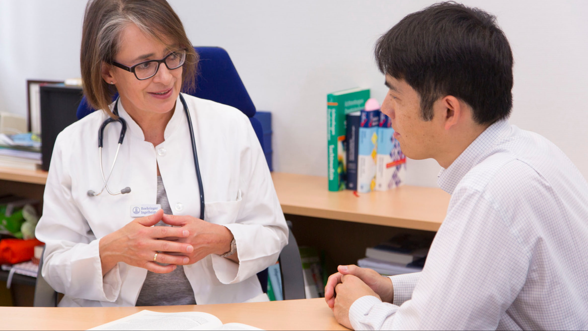 Docteure parle en regardant un patient dans les yeux, tous deux sont assis devant divers documents